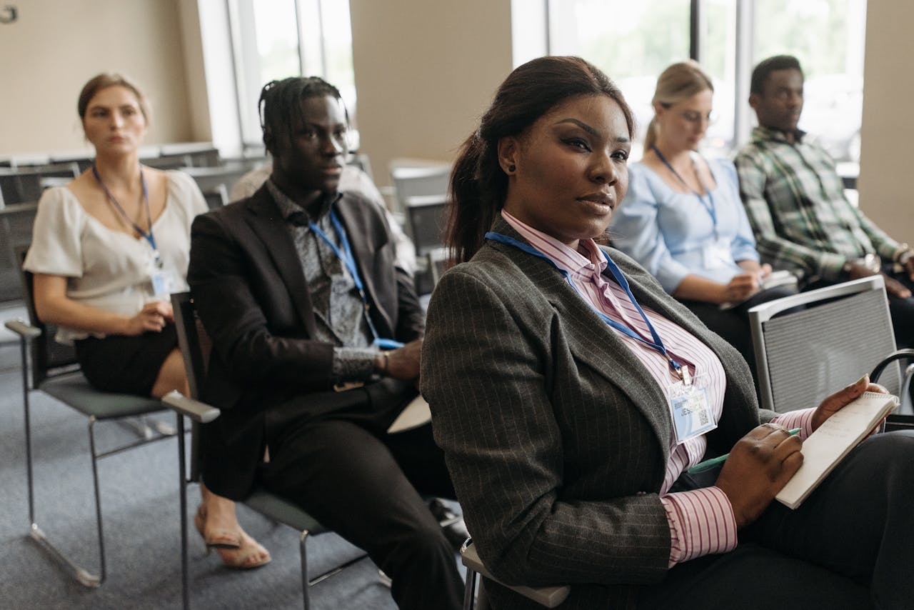 gallery-05 A diverse group attentively listens in a business seminar setting, indoors with notebooks.